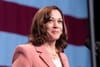 Kamala Harris in a pink jacket and pearls, with an American flag behind her